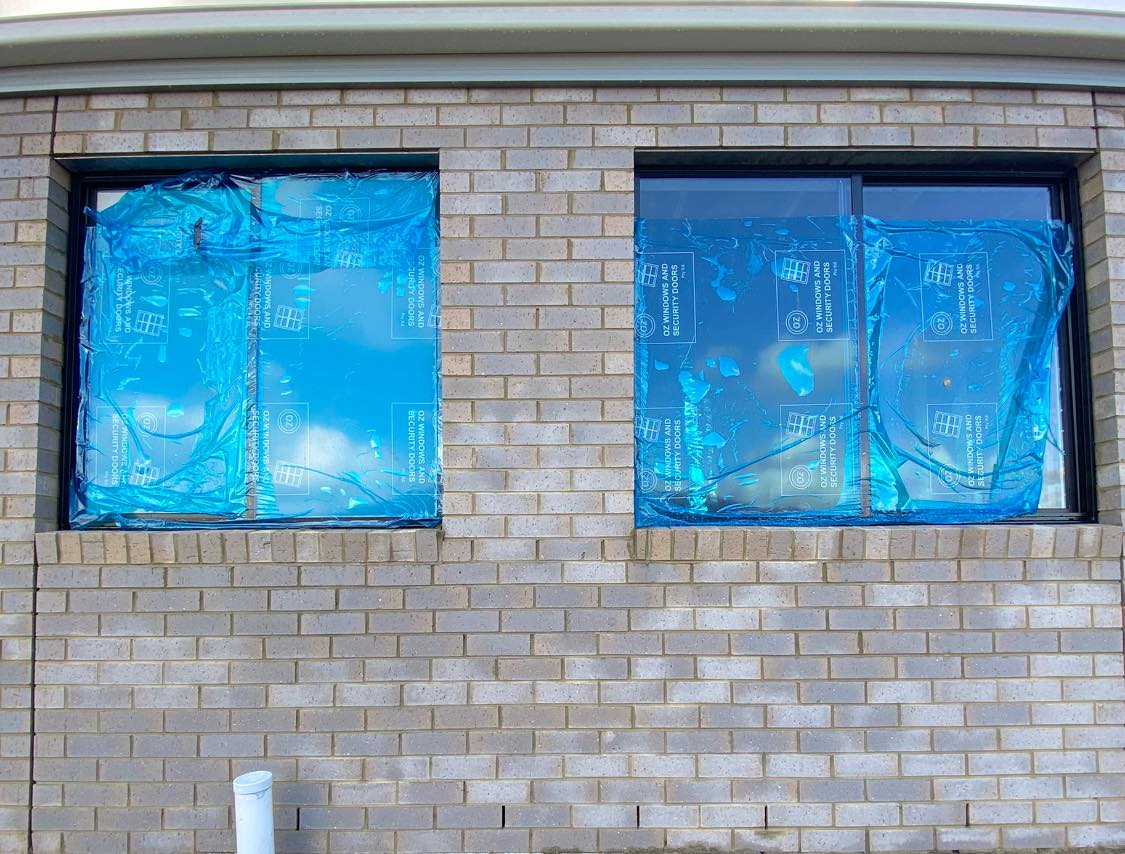 Cream brick wall with grey mortar haze under plastic-wrapped windows on a new build.