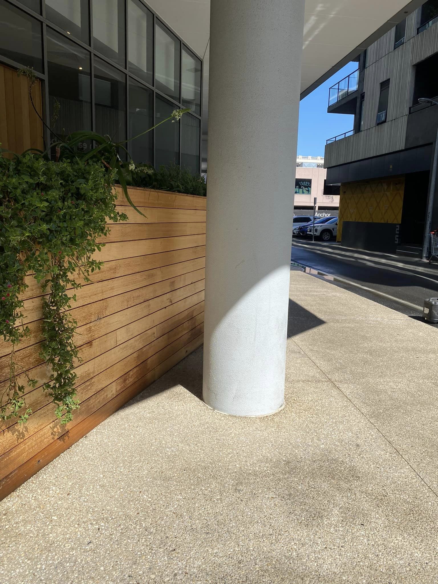Exposed aggregate concrete forecourt beside a round column at a mixed-use building.