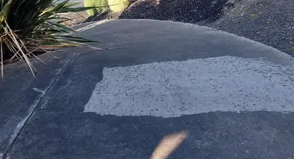 Concrete driveway with a pale cleaned test patch in the darker untreated surface.