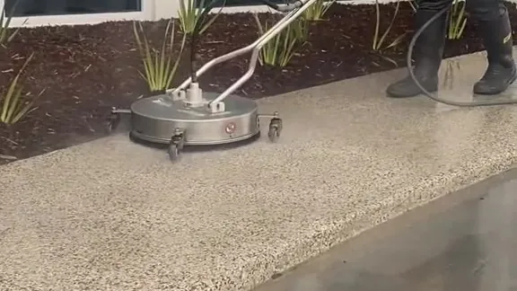 Spotless operator running a surface cleaner over an exposed aggregate path