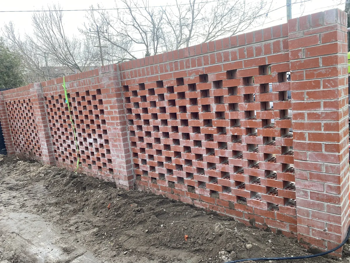 Red clay brick fence with open breeze-block panels on a building site.